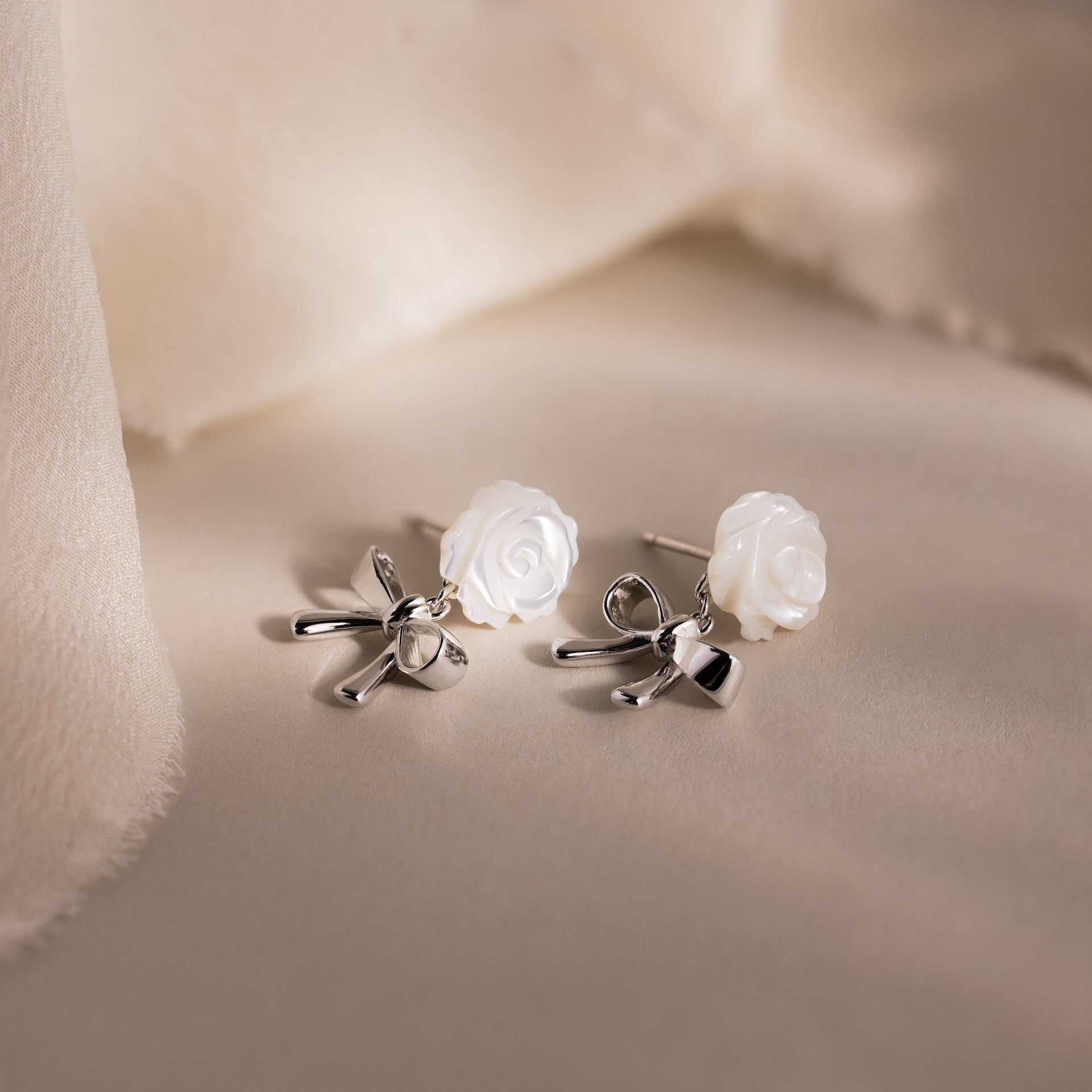 White rose and silver bow earrings displayed on a neutral surface.