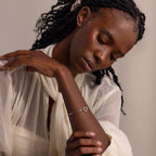 Model wearing a silver heart bracelet with a paperclip chain, styled with a sheer cream blouse and resting her arm gently across her chest.