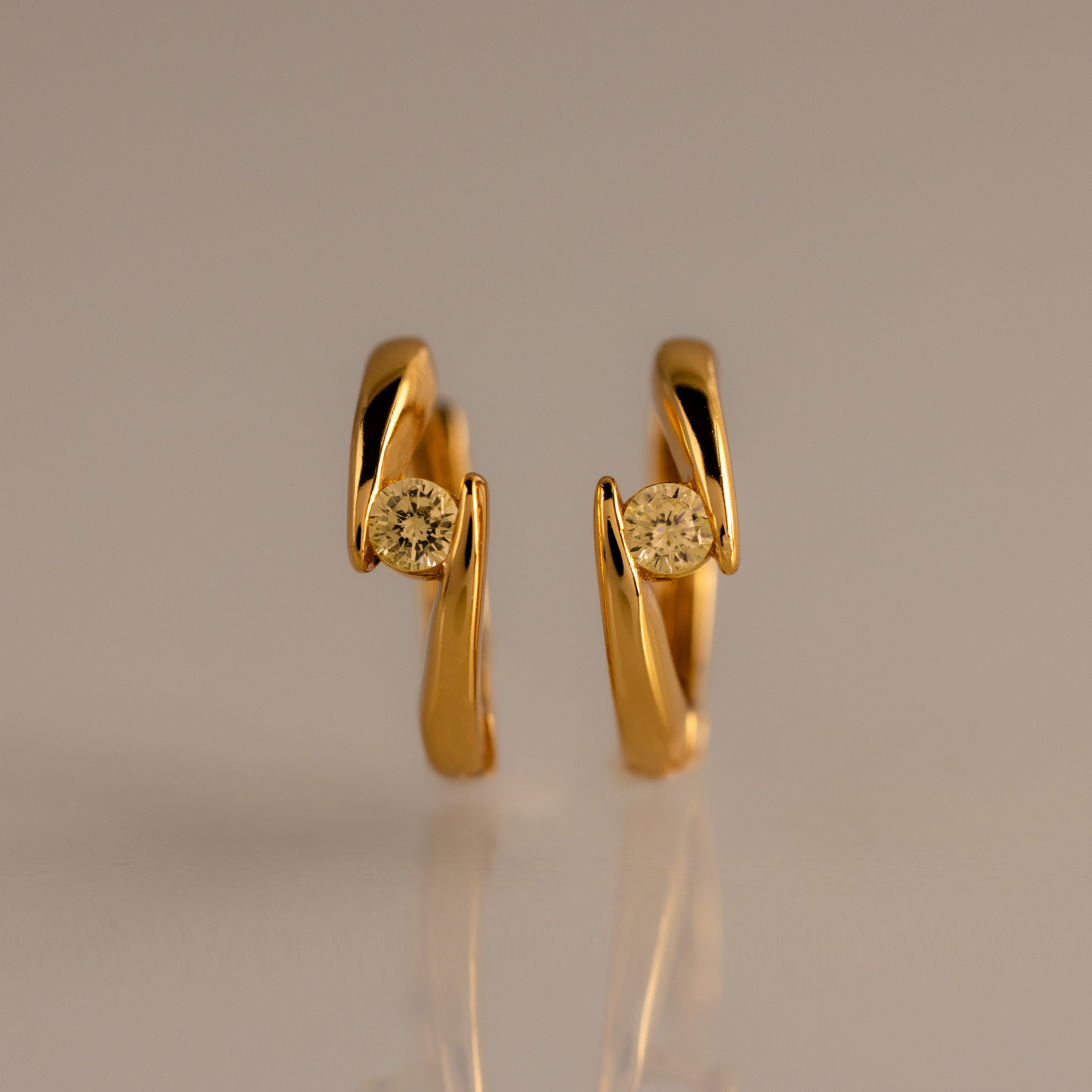 Floating Topaz Huggies: Gold hoop earrings with a curved design, each featuring a round yellow topaz at the center, shown on a neutral background.