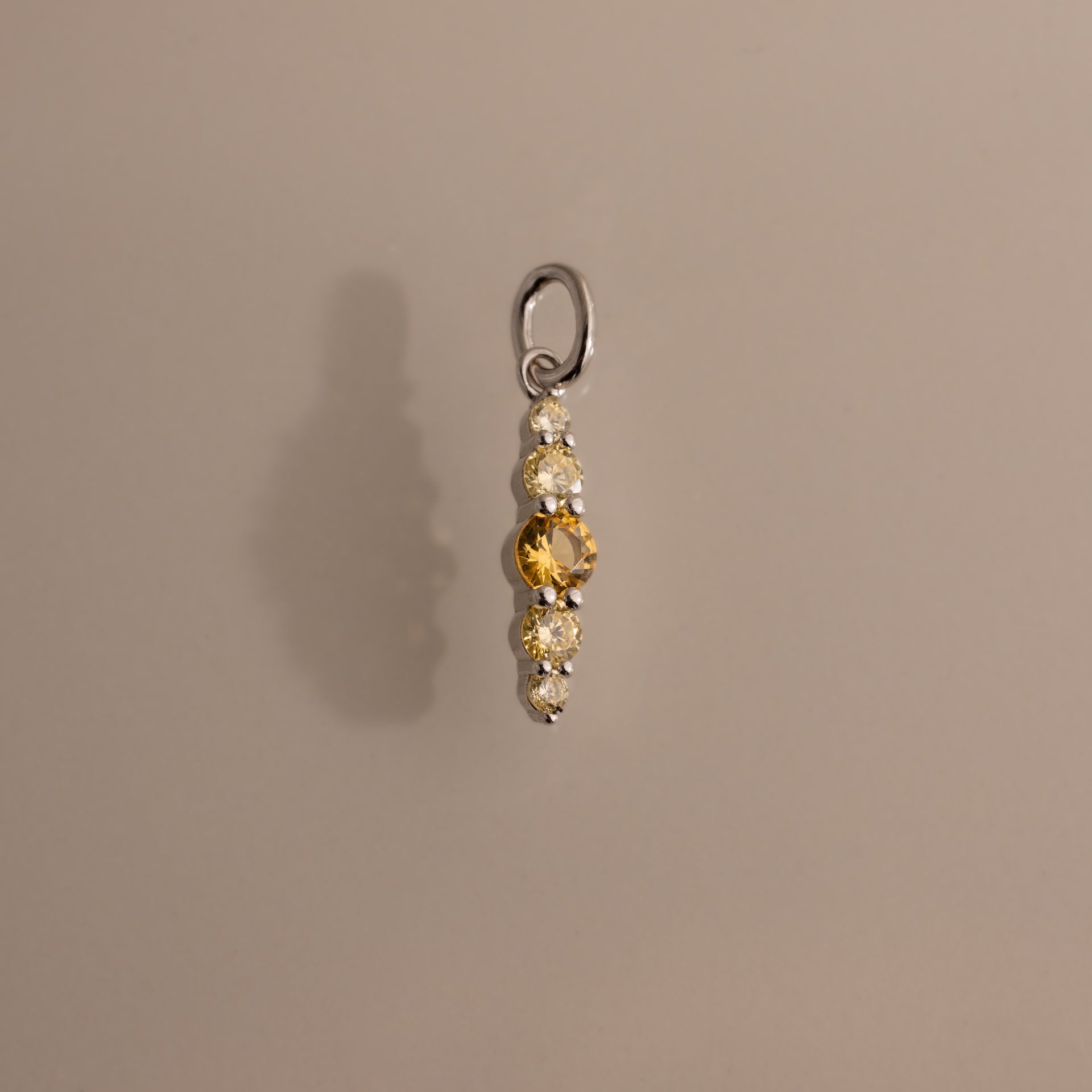 The Ombre Lace Topaz Charm features a central yellow gemstone accented by three clear stones on each side, set in metal—a personalized charm ideal for any occasion.