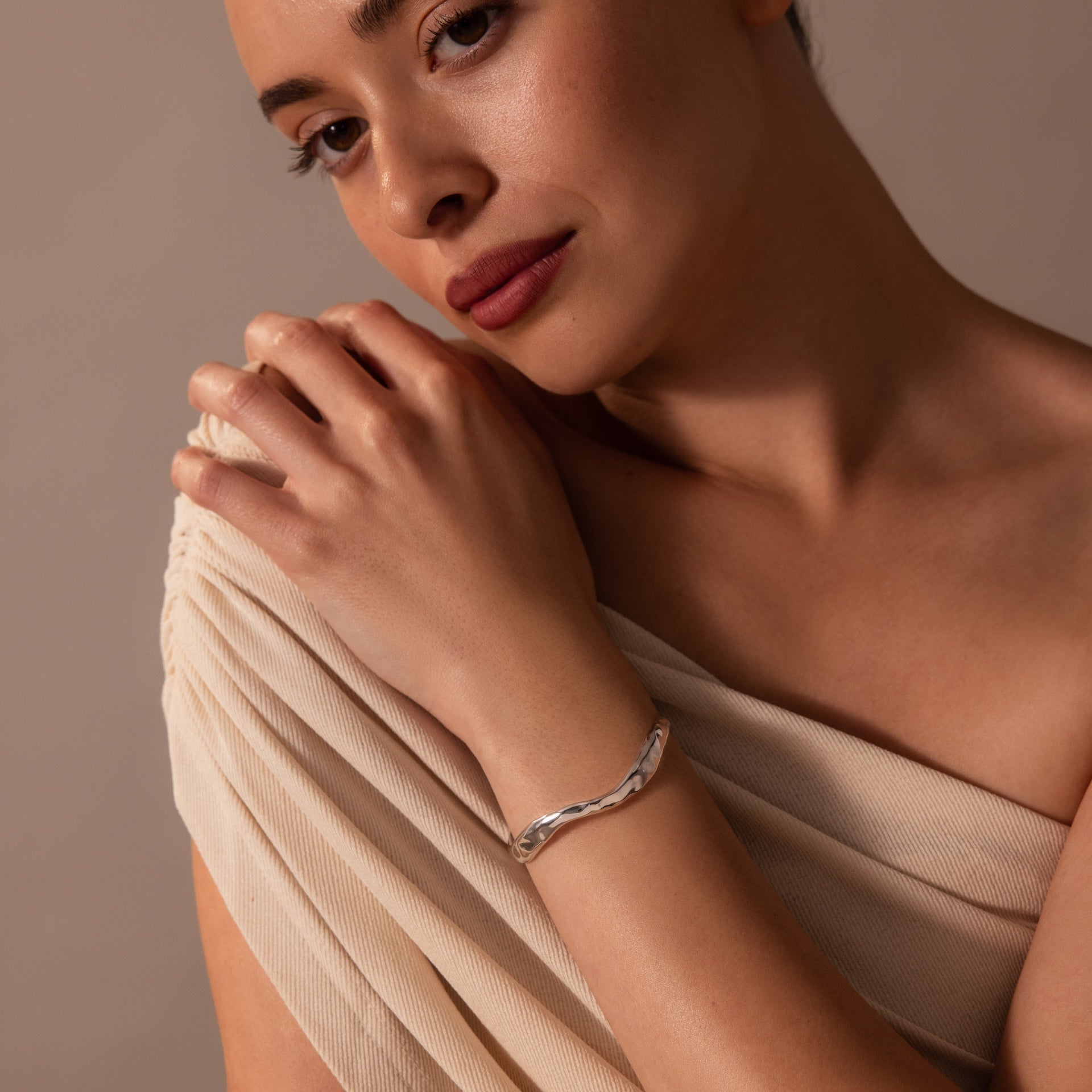 A woman in a cream dress poses with her hand on her shoulder, showcasing the Organic Wavy Cuff Bracelet with its sculpted curves and textured finish.