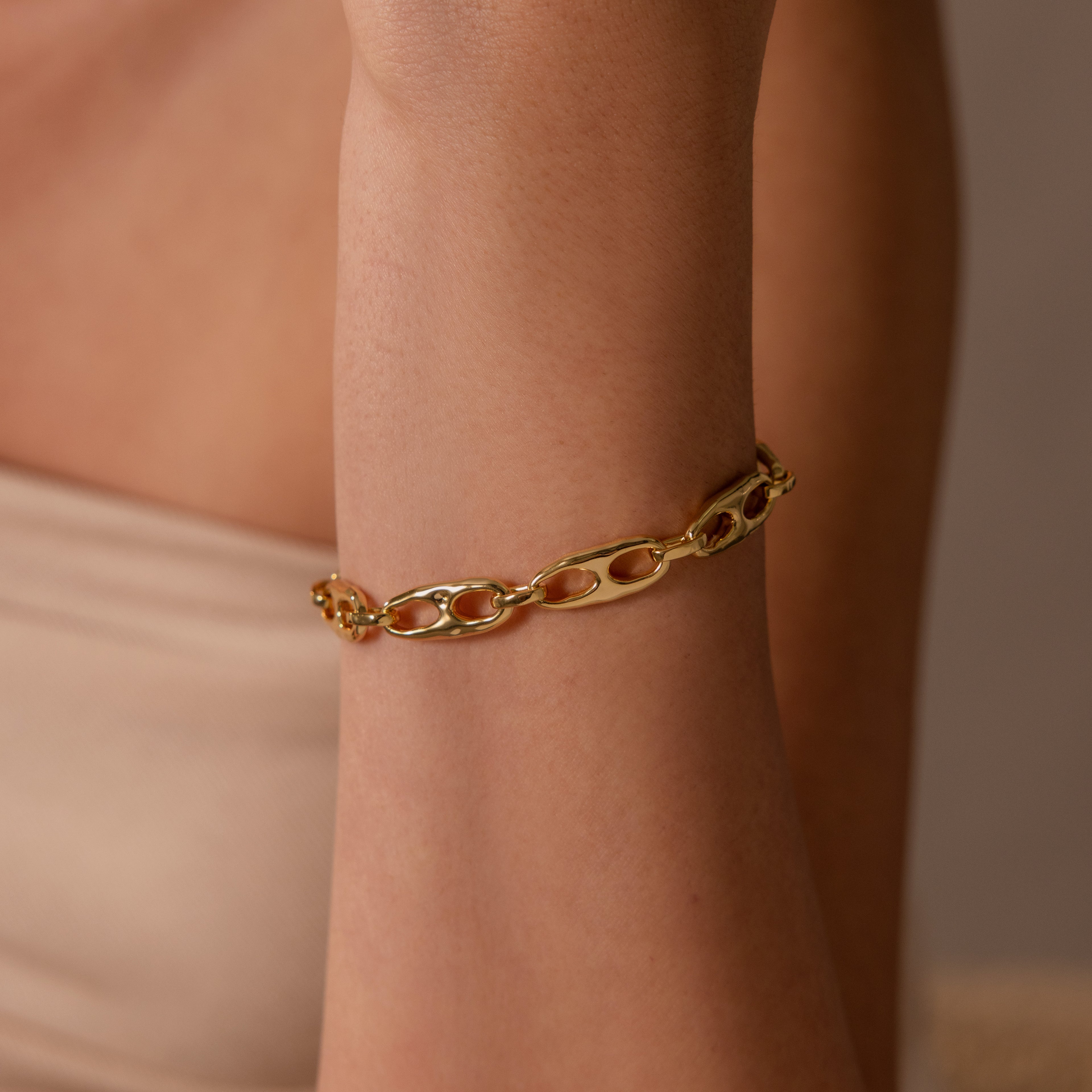 The Organic Mariner Chain Bracelet in 18K Gold shines on the wrist, its sculptural links glowing against smooth skin and a beige backdrop—a timeless essential for any jewelry collection.