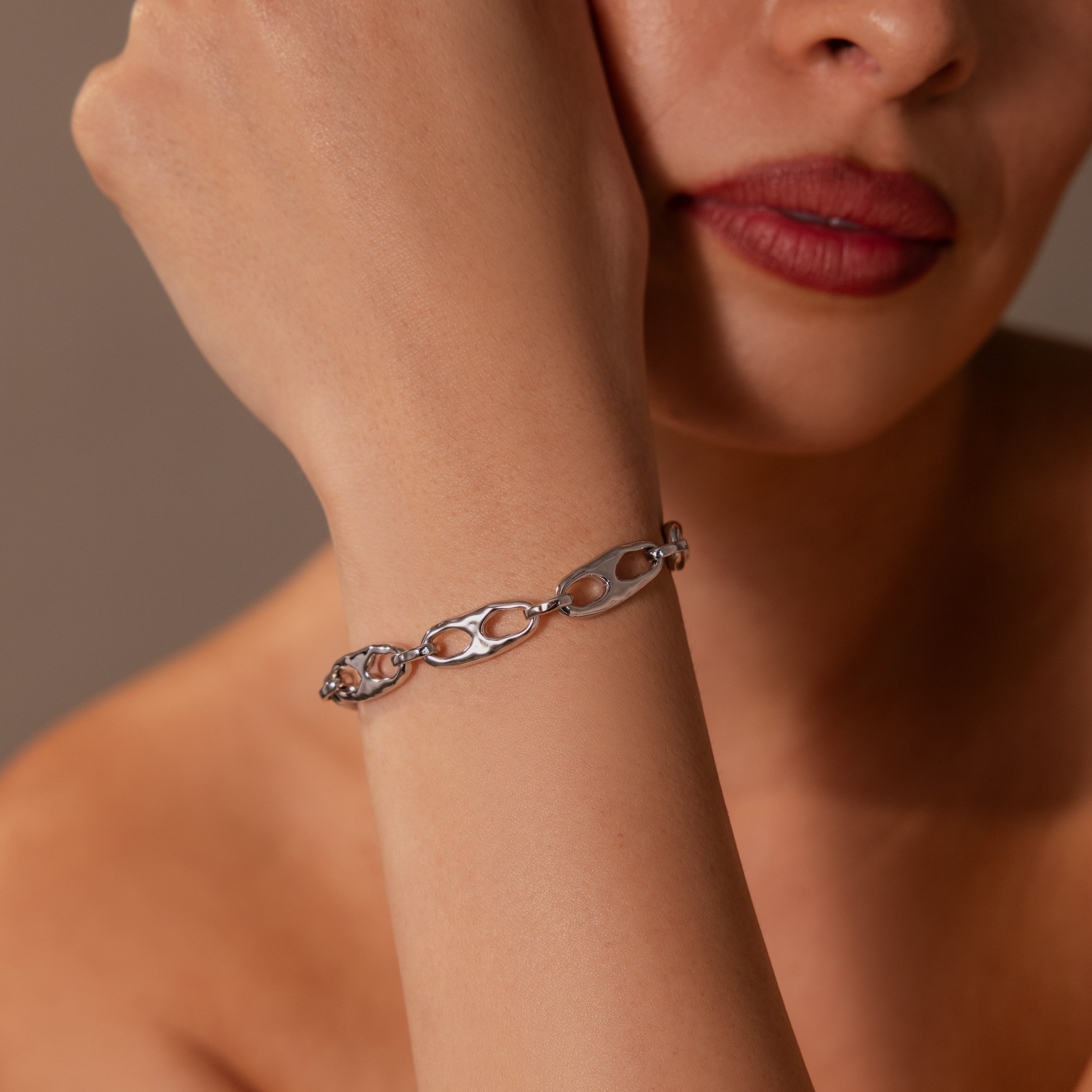 A woman with red lipstick wears the Organic Mariner Chain Bracelet in Silver, resting her hand on her chin—a sculptural piece that creates a timeless, striking statement.