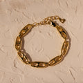 Timeless essential: the Organic Mariner Chain Bracelet in 18K Gold features elegant oval links, beautifully displayed on a textured beige surface.