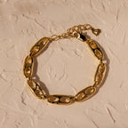 Timeless essential: the Organic Mariner Chain Bracelet in 18K Gold features elegant oval links, beautifully displayed on a textured beige surface.