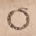 The Organic Mariner Chain Bracelet in Silver, featuring oval links, is displayed on a textured beige surface, offering a timeless style perfect for any occasion.