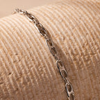 The Organic Mariner Chain Bracelet in Silver features sculptural oval links, elegantly displayed on a textured beige surface.