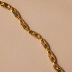 The Organic Mariner Chain Bracelet in 18K Gold features sculptural oval links arranged diagonally, creating a timeless and elegant design against a beige background.