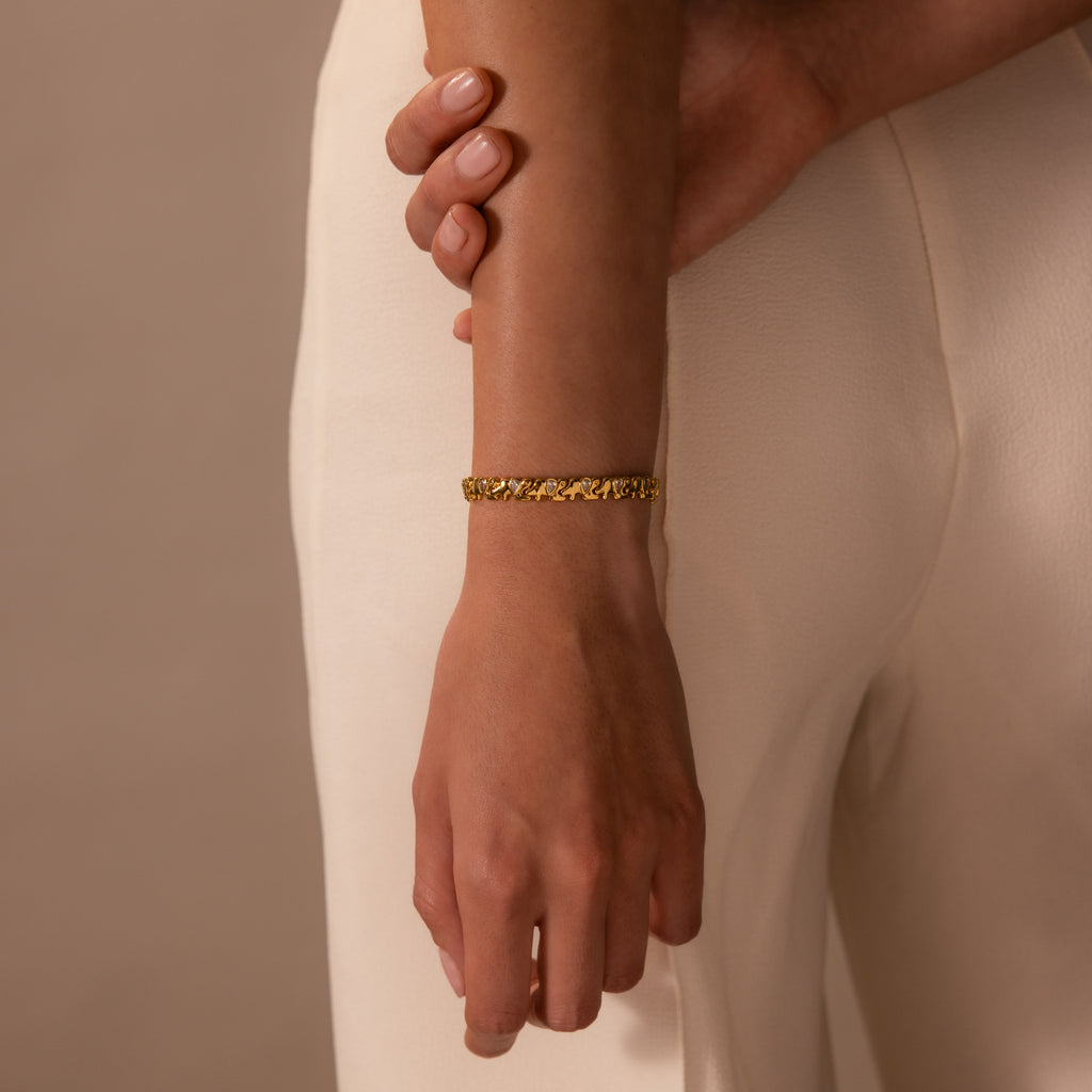 A person wearing a Diamond Elephant Link Bracelet and cream-colored pants, with one hand gently holding their arm.