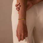 A person wearing a Diamond Elephant Link Bracelet and cream-colored pants, with one hand gently holding their arm.