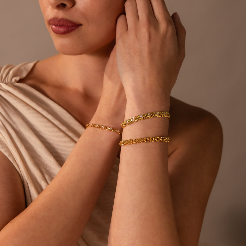 A woman in a beige top wears two gold bracelets on her wrist, including the Diamond Elephant Link Bracelet, with soft lighting and a neutral background.