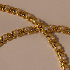 Gold bracelets with repeating chameleon motifs and teardrop crystals rest on a beige surface beside the Diamond Elephant Link Bracelet, creating an elegant, animal-inspired ensemble.