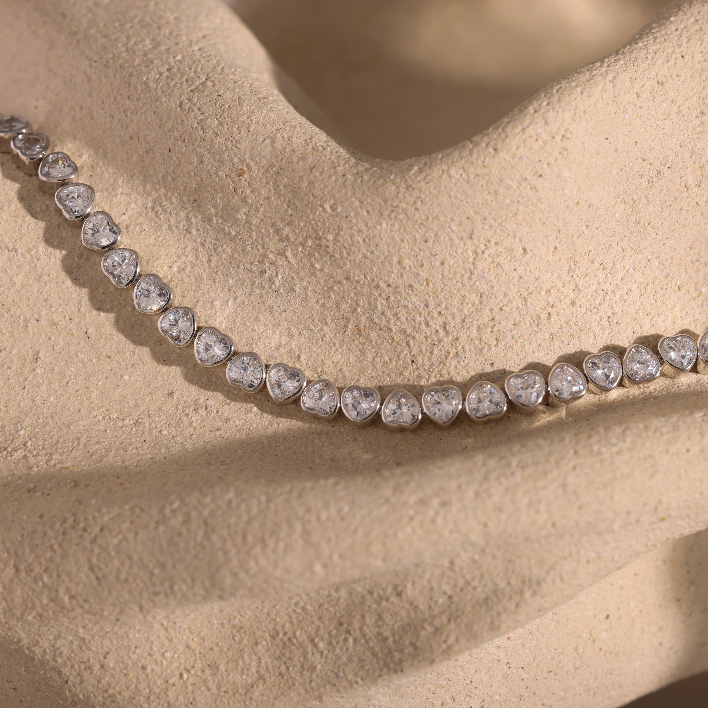 A Heart Tennis Bracelet in Silver, radiating timeless beauty, is displayed on a textured beige fabric background.