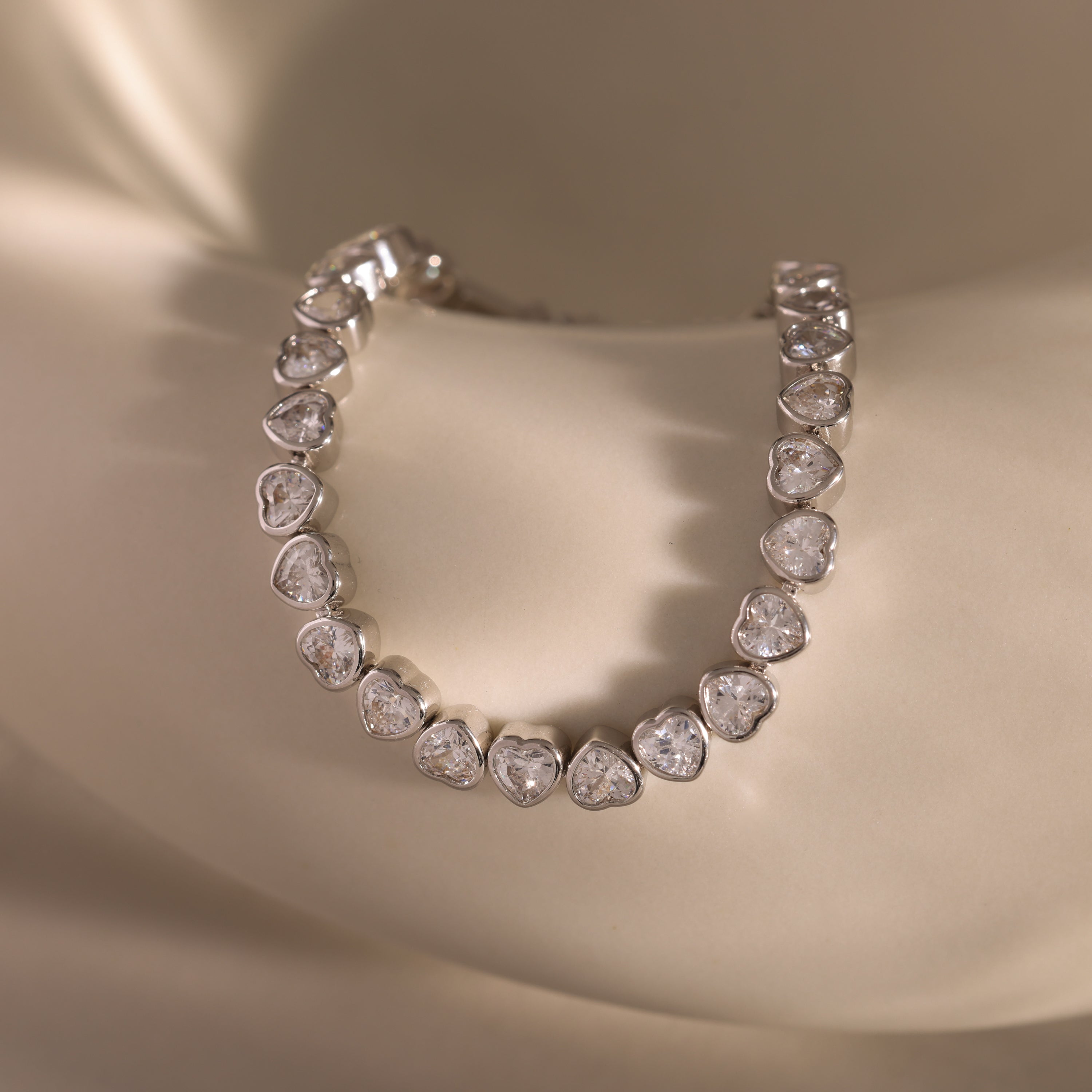 The Heart Tennis Bracelet in Silver features elegant heart-shaped stones, showcasing timeless beauty against a smooth, light-colored background.