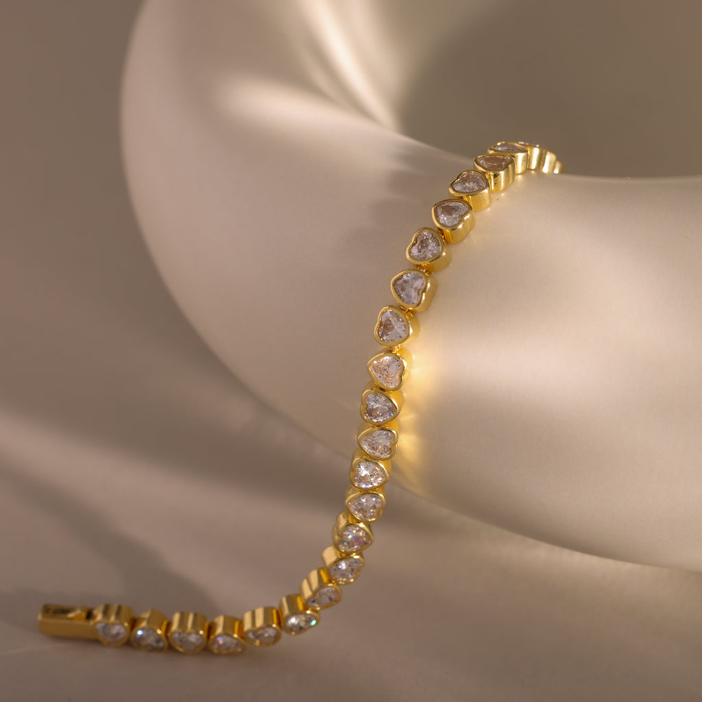 The Heart Tennis Bracelet in 18K Gold, featuring teardrop-shaped diamonds, drapes elegantly over a soft matte white ceramic bowl—an exquisite piece of fine jewelry.