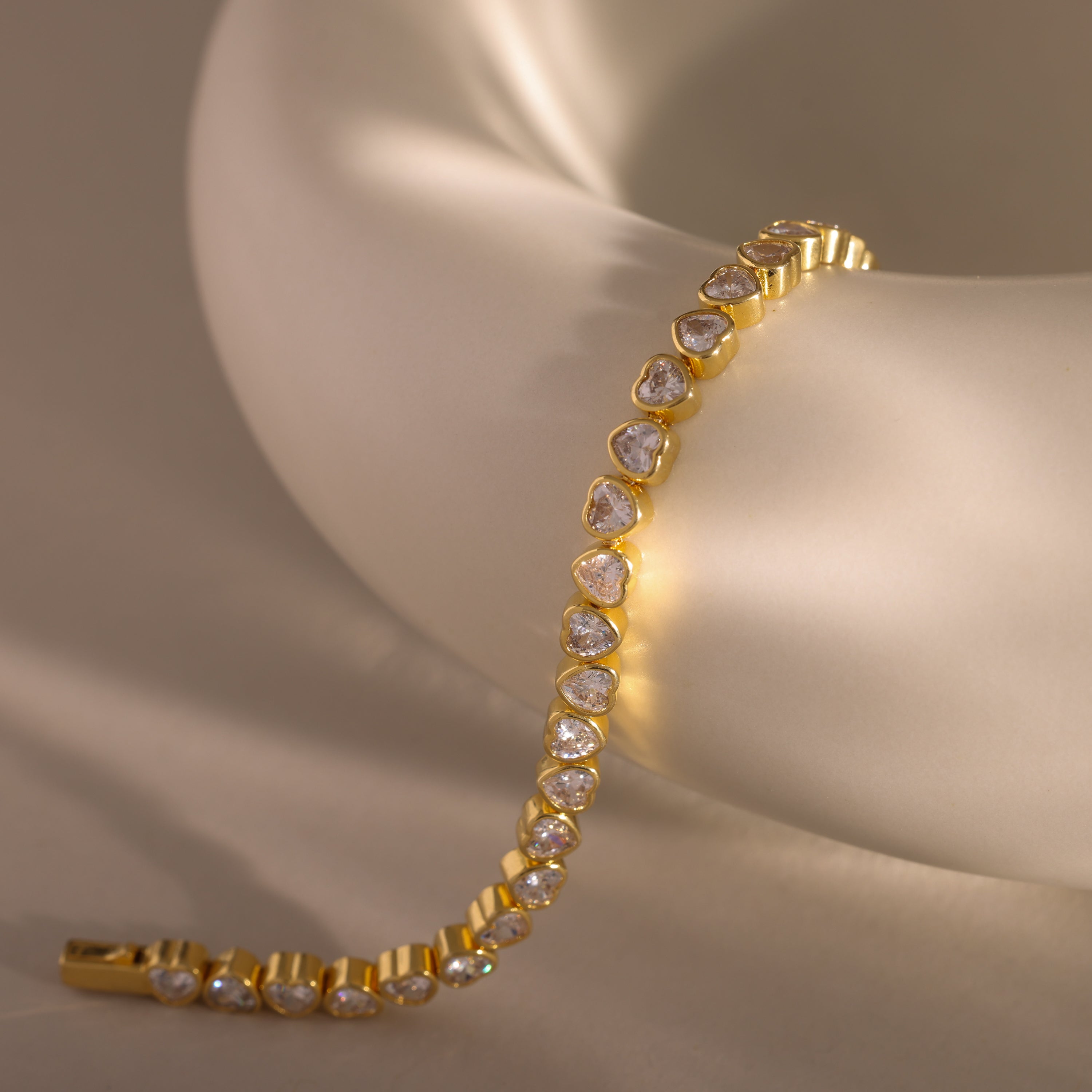 The Heart Tennis Bracelet in 18K Gold, featuring teardrop-shaped diamonds, drapes elegantly over a soft matte white ceramic bowl—an exquisite piece of fine jewelry.