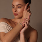 A woman in an off-shoulder top touches her face while wearing the Heart Tennis Bracelet in Silver, adorned with heart-shaped stones, and looks to the side with timeless elegance.