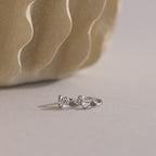 Pair of silver Pave Viper Huggie earrings with a wavy snake-like design and marquise stones, placed on a neutral surface near a textured vase.