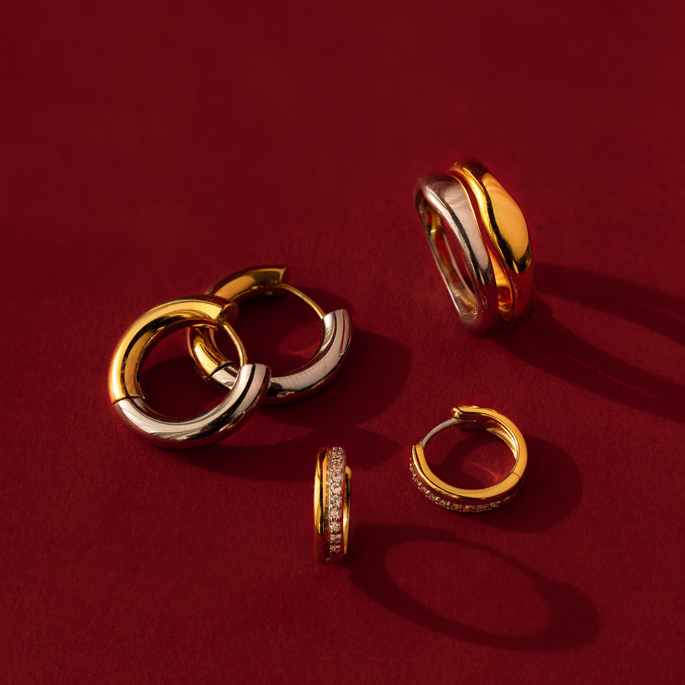 The Duo Form Ring Set in Silver is elegantly displayed on a rich red background, capturing sculptural style in gleaming hoops and rings.