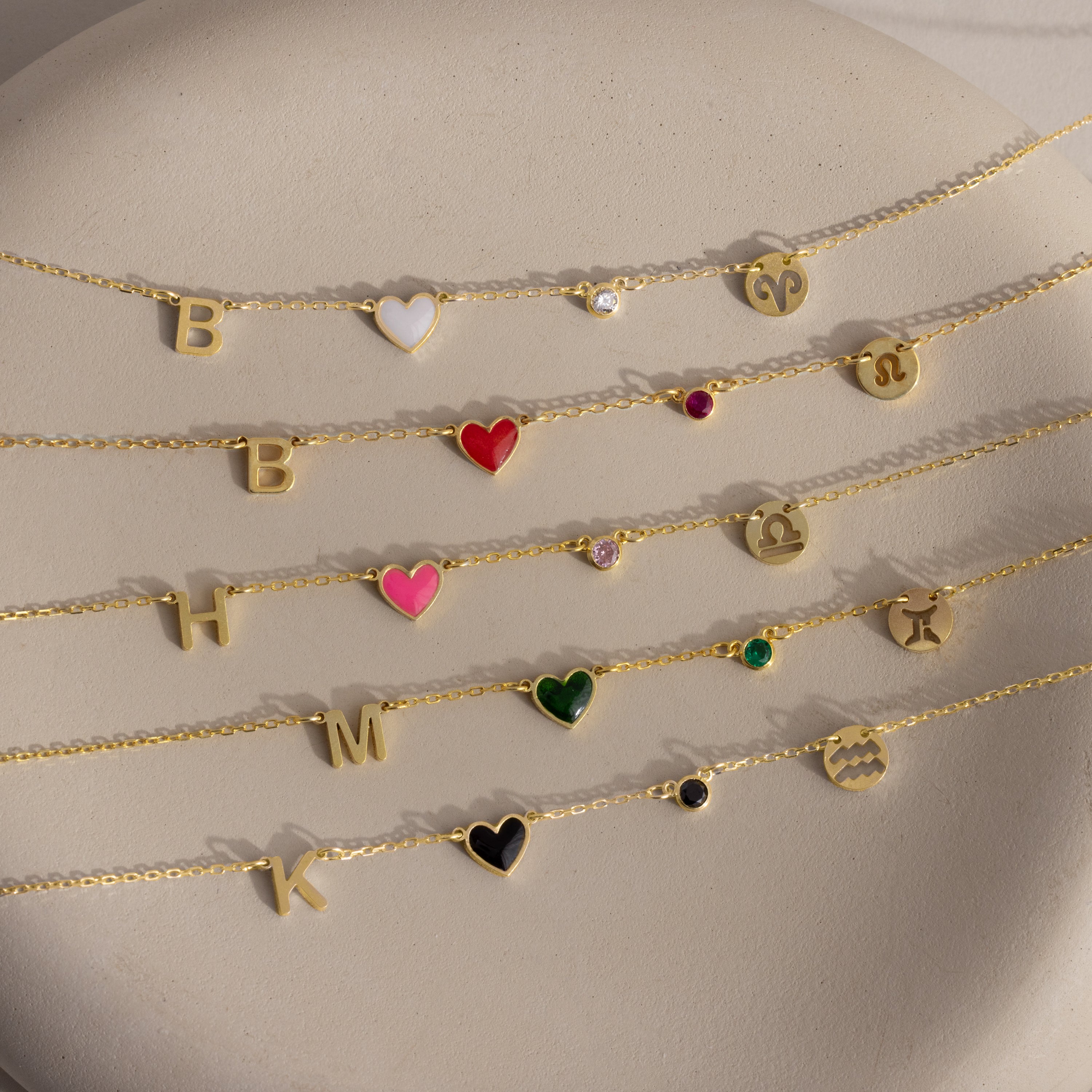 Five gold chain bracelets featuring letter, heart, gemstone, and zodiac charms are displayed on a light stone surface—perfect for pairing with the Dainty Space Charm Necklace or other personalized jewelry for a unique touch.