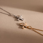 The Art Deco Cross Necklace features silver and gold finishes with gemstone centers, shining on a beige background—ideal for vintage necklace lovers.