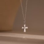 The Art Deco Cross Necklace in Silver features a diamond-studded pendant with sparkling baguette stones, showcased against a neutral background.