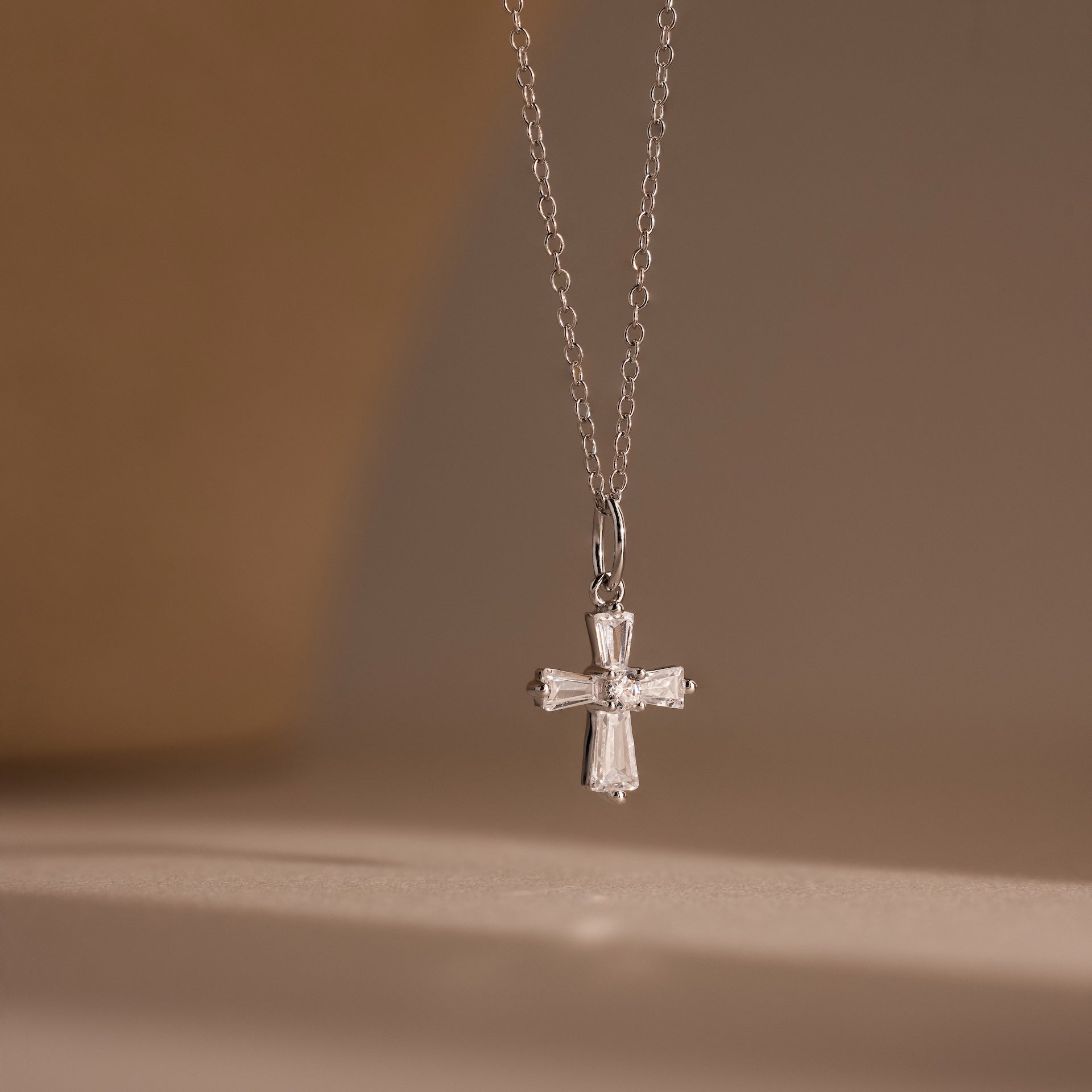 The Art Deco Cross Necklace in Silver features a diamond-studded pendant with sparkling baguette stones, showcased against a neutral background.