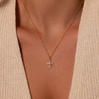 The Art Deco Cross Necklace in 18K Gold, featuring sparkling baguette stones, rests elegantly on a cream knit top, adding vintage charm to any outfit.