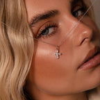 A close-up of a woman with blonde hair wearing the Art Deco Cross Necklace in Silver, adorned with baguette stones and elegantly draped across her face, showcasing the vintage charm of this jewelry piece.
