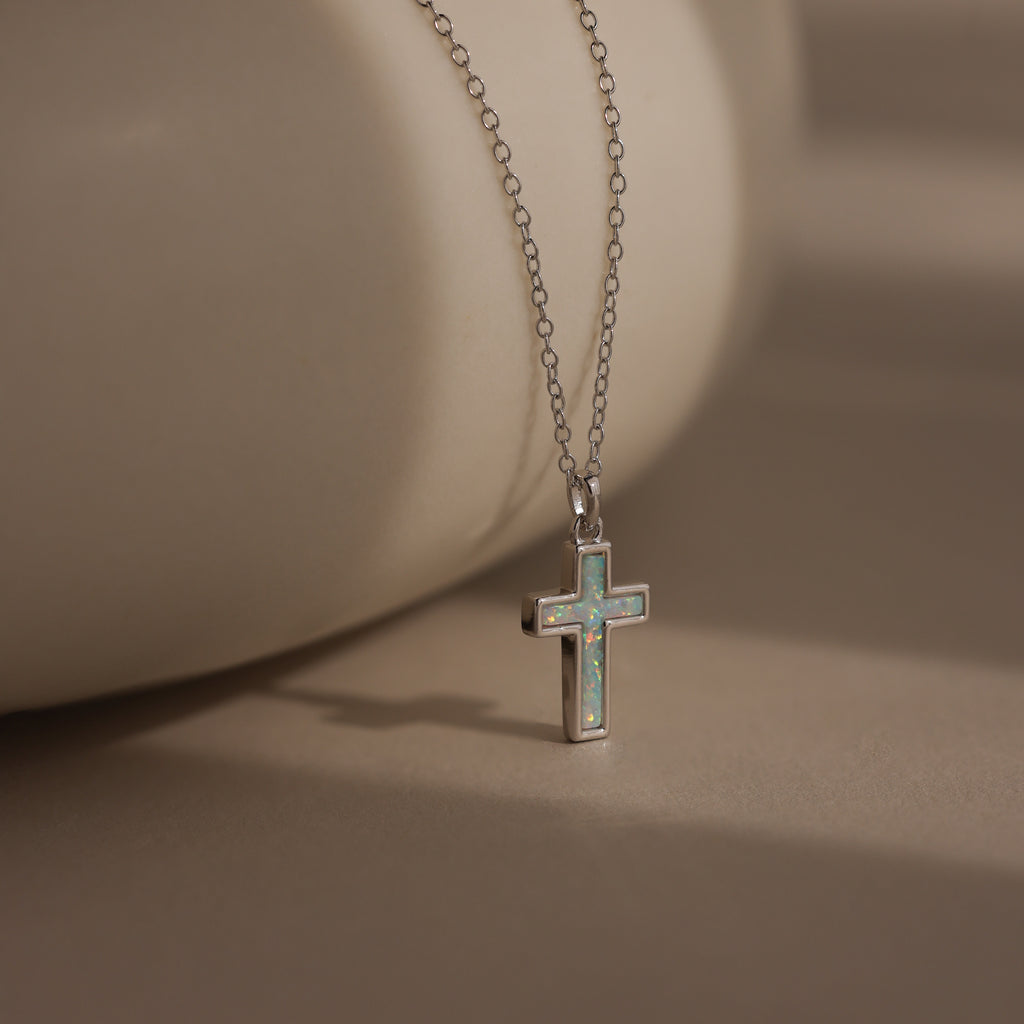 The Mother of Pearl Cross Necklace in Silver features an iridescent inlay pendant on a delicate chain, making it a timeless piece that shines beautifully against any neutral background.