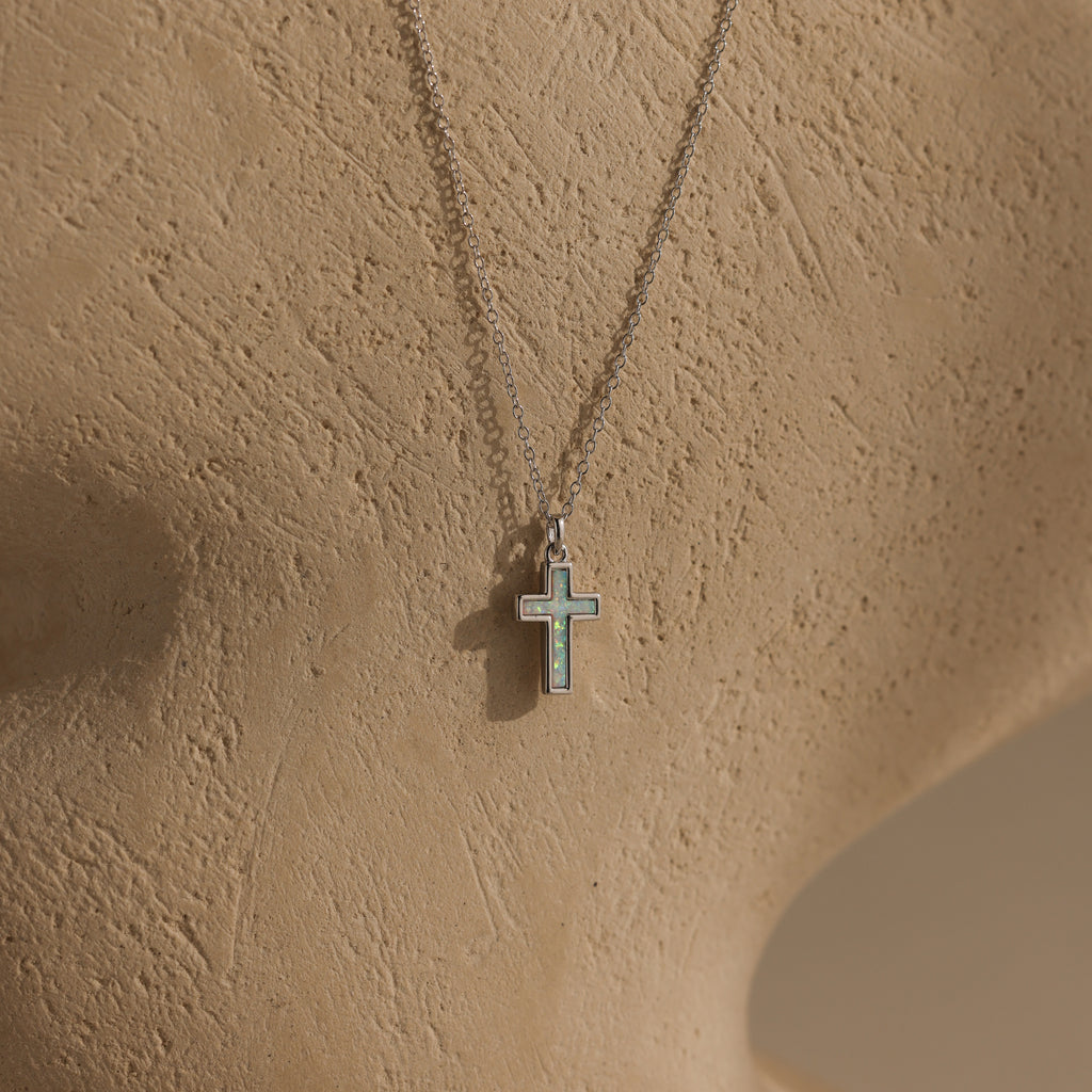 The Mother of Pearl Cross Necklace in Silver features an iridescent inlay pendant and is displayed on a textured beige mannequin bust—a timeless piece that brings elegance to any style.