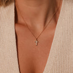 The Mother of Pearl Cross Necklace in 18K Gold graces her neck, its shimmering inlay standing out against a cream knit V-neck top—a refined statement of timeless elegance.