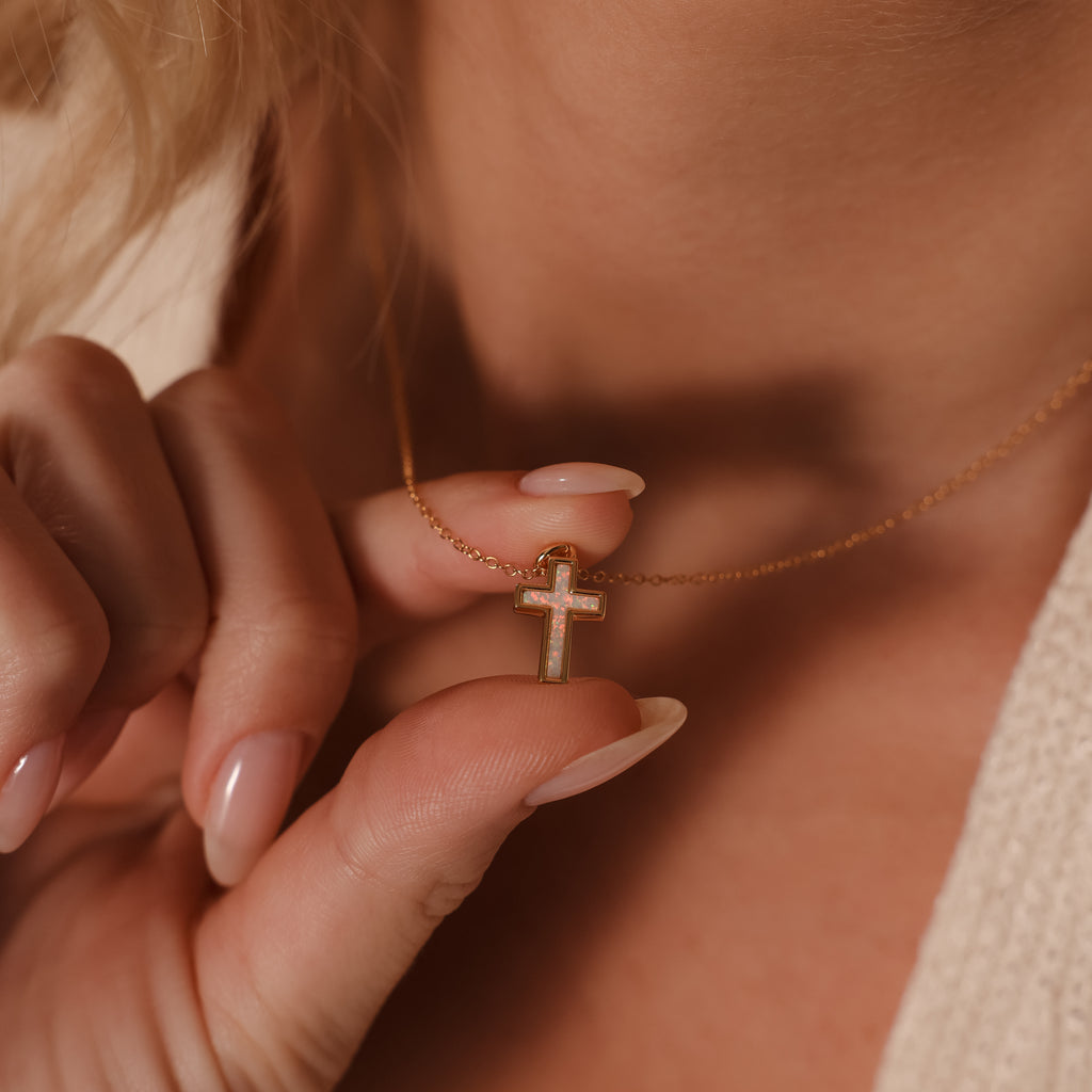 Close-up of a woman holding the Mother of Pearl Cross Necklace in 18K Gold, showcasing its delicate design and iridescent inlay—a timeless jewelry piece.