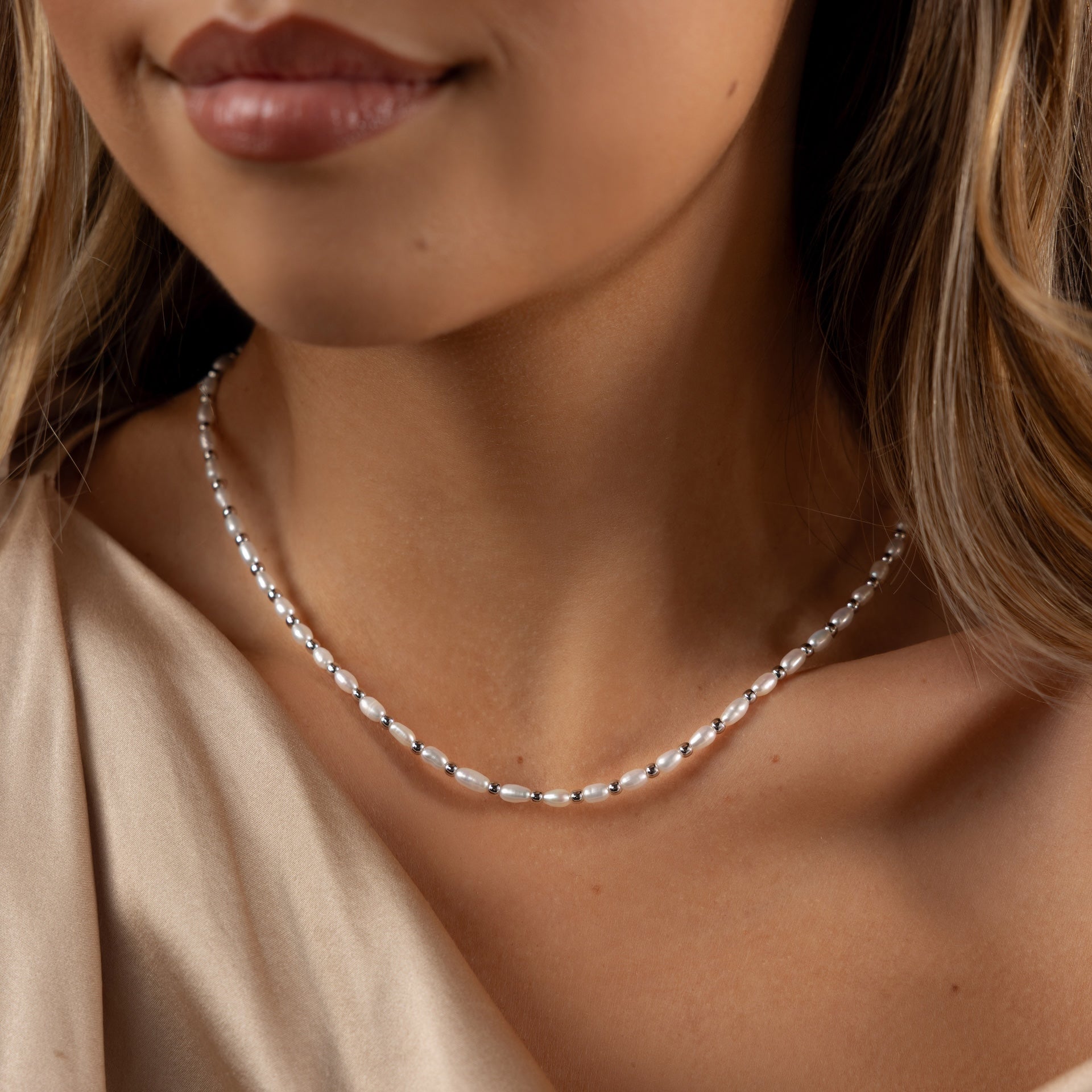 A woman wearing the Beaded Pearl Necklace in White Gold with freshwater pearls and a cream-colored top.
