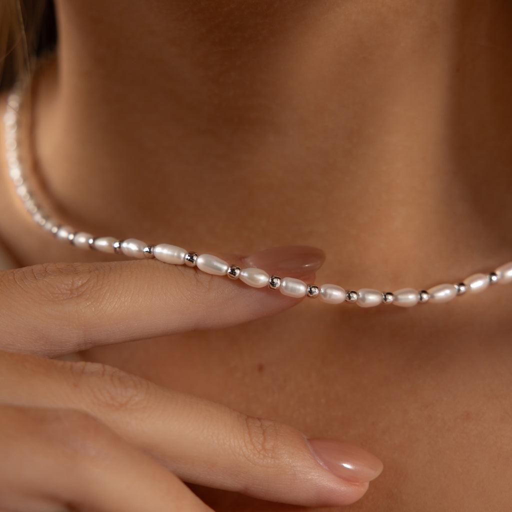 A close-up of a hand touching the Beaded Pearl Necklace in White Gold, featuring freshwater pearls and polished beads, resting elegantly on a person's neck.