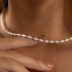 A close-up of a hand touching the Beaded Pearl Necklace in White Gold, featuring freshwater pearls and polished beads, resting elegantly on a person's neck.