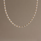 The Beaded Pearl Necklace in 18K Gold showcases alternating small freshwater pearls and polished gold beads, set against a plain beige background.