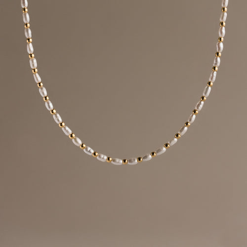 The Beaded Pearl Necklace in 18K Gold showcases alternating small freshwater pearls and polished gold beads, set against a plain beige background.