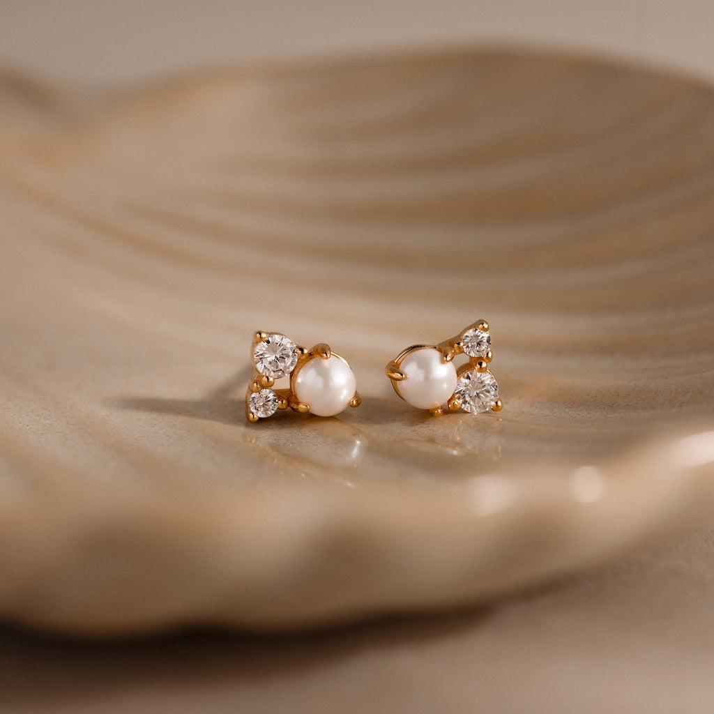 The Pearl Diamond Cluster Studs in 18K Gold feature pearls and diamonds for everyday elegance, shown resting gracefully on a beige ceramic dish.