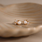 The Pearl Diamond Cluster Studs in 18K Gold feature pearls and diamonds for everyday elegance, shown resting gracefully on a beige ceramic dish.