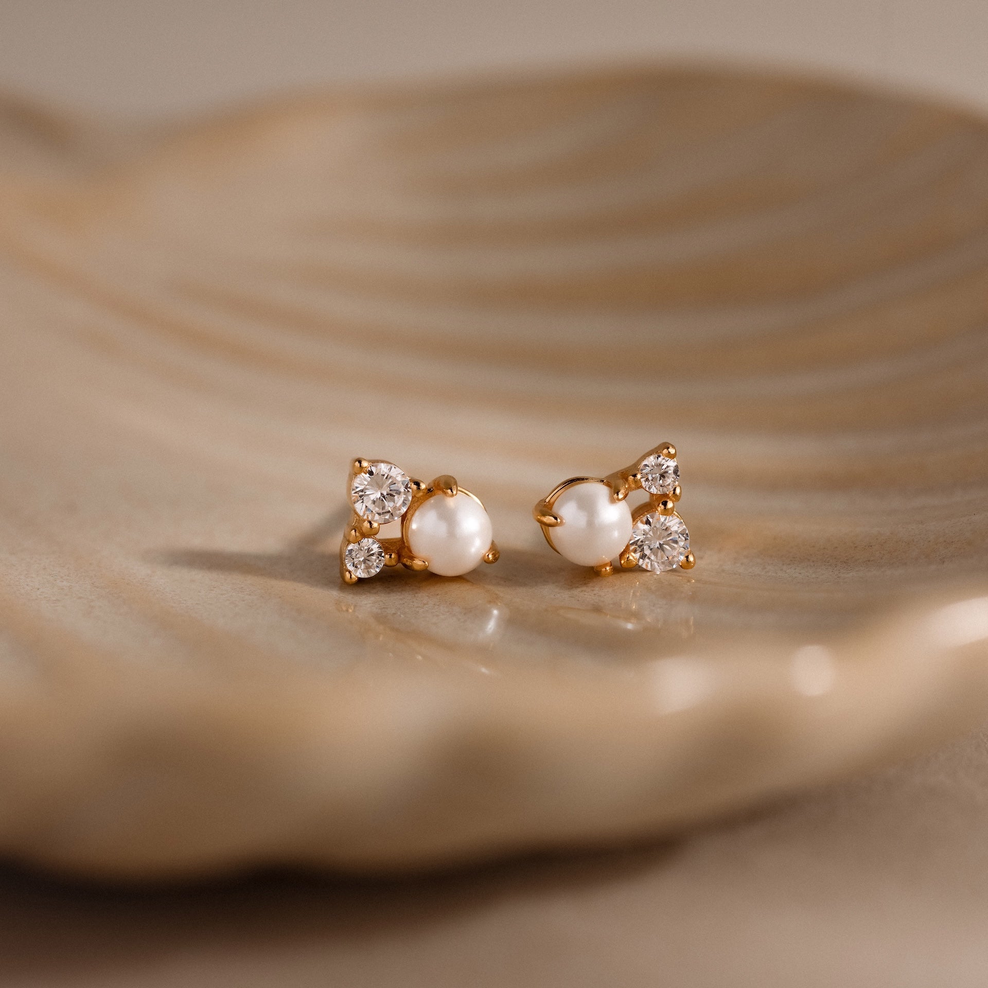 The Pearl Diamond Cluster Studs in 18K Gold feature pearls and diamonds for everyday elegance, shown resting gracefully on a beige ceramic dish.