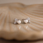 The Pearl Diamond Cluster Studs in Sterling Silver are displayed on a textured, beige seashell surface.
