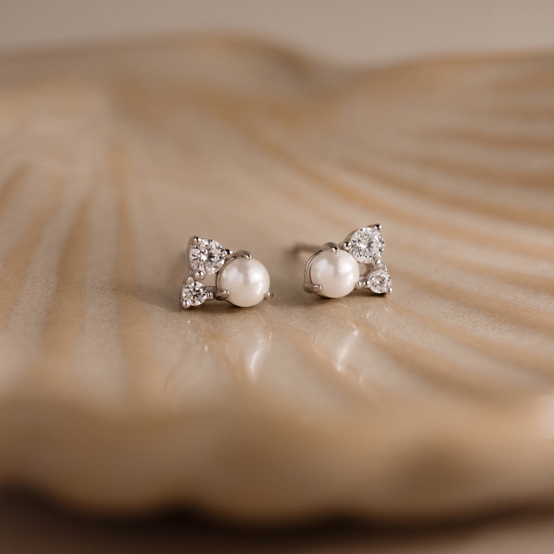 The Pearl Diamond Cluster Studs, adorned with sparkling CZ diamond accents, rest elegantly on a shell.