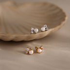 The Pearl Diamond Cluster Studs, available in gold and silver, showcase CZ diamond accents and pearls, elegantly displayed on and near a shell dish.