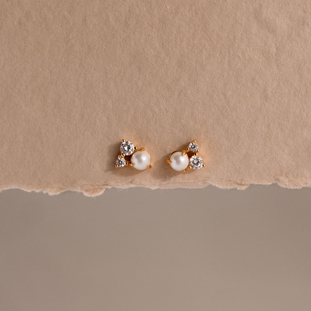 Pearl Diamond Cluster Studs in 18K Gold with pearls and small crystals rest on a textured beige background—elegant stud earrings for everyday wear.