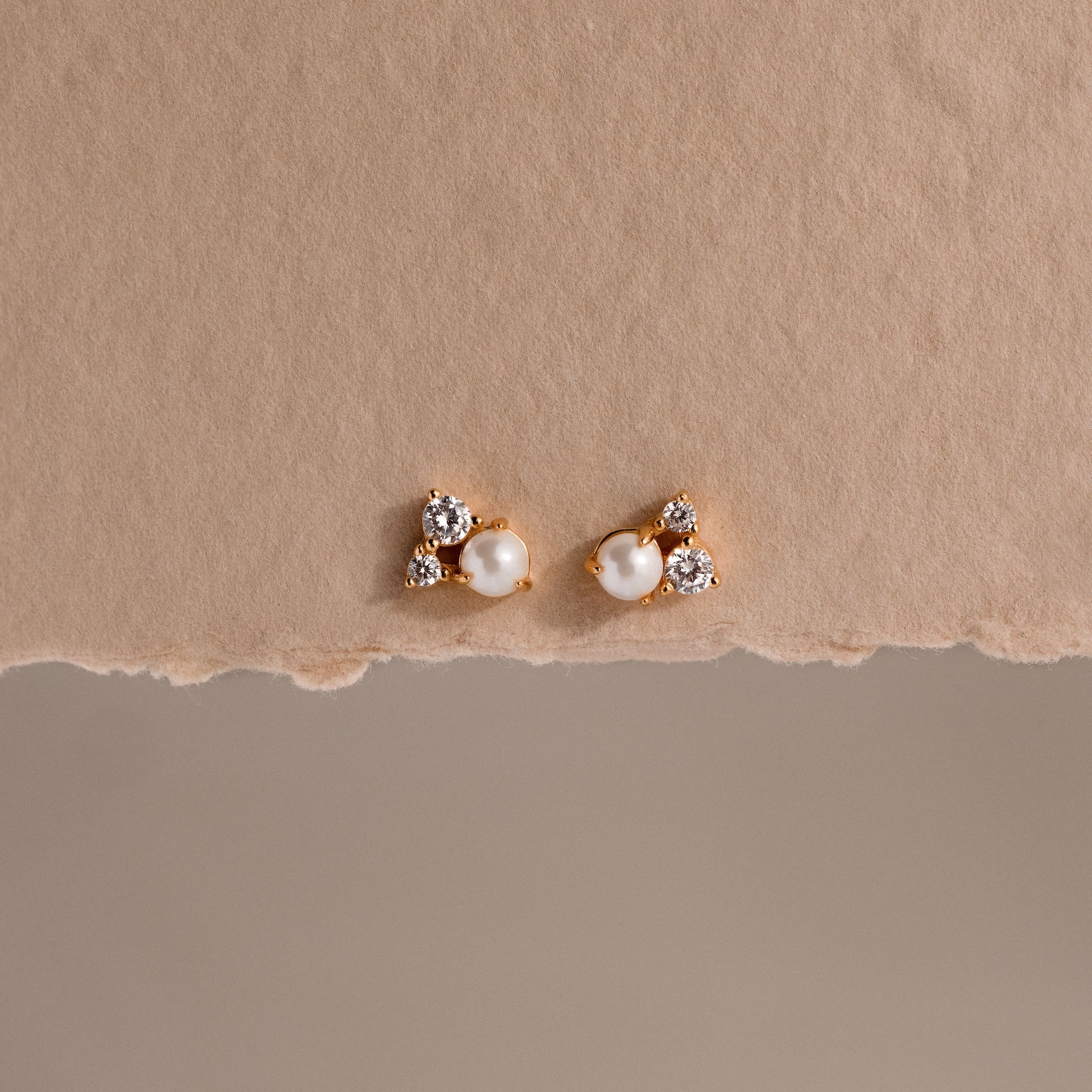 Pearl Diamond Cluster Studs in 18K Gold with pearls and small crystals rest on a textured beige background—elegant stud earrings for everyday wear.