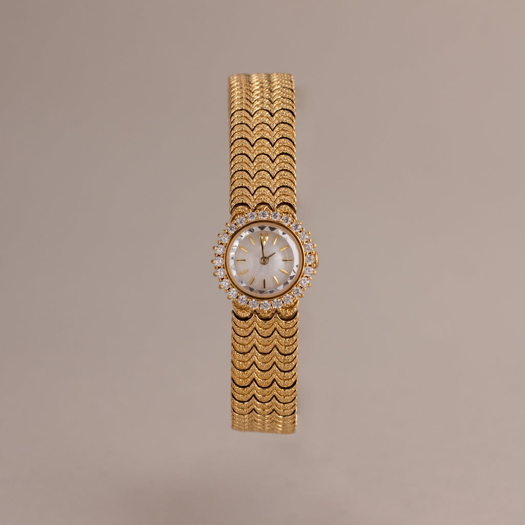 The Pave Scalloped Timepiece features a round face, diamond accents, and a scallop-link bracelet set against a neutral background.