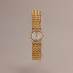 The Pave Scalloped Timepiece features a round face, diamond accents, and a scallop-link bracelet set against a neutral background.