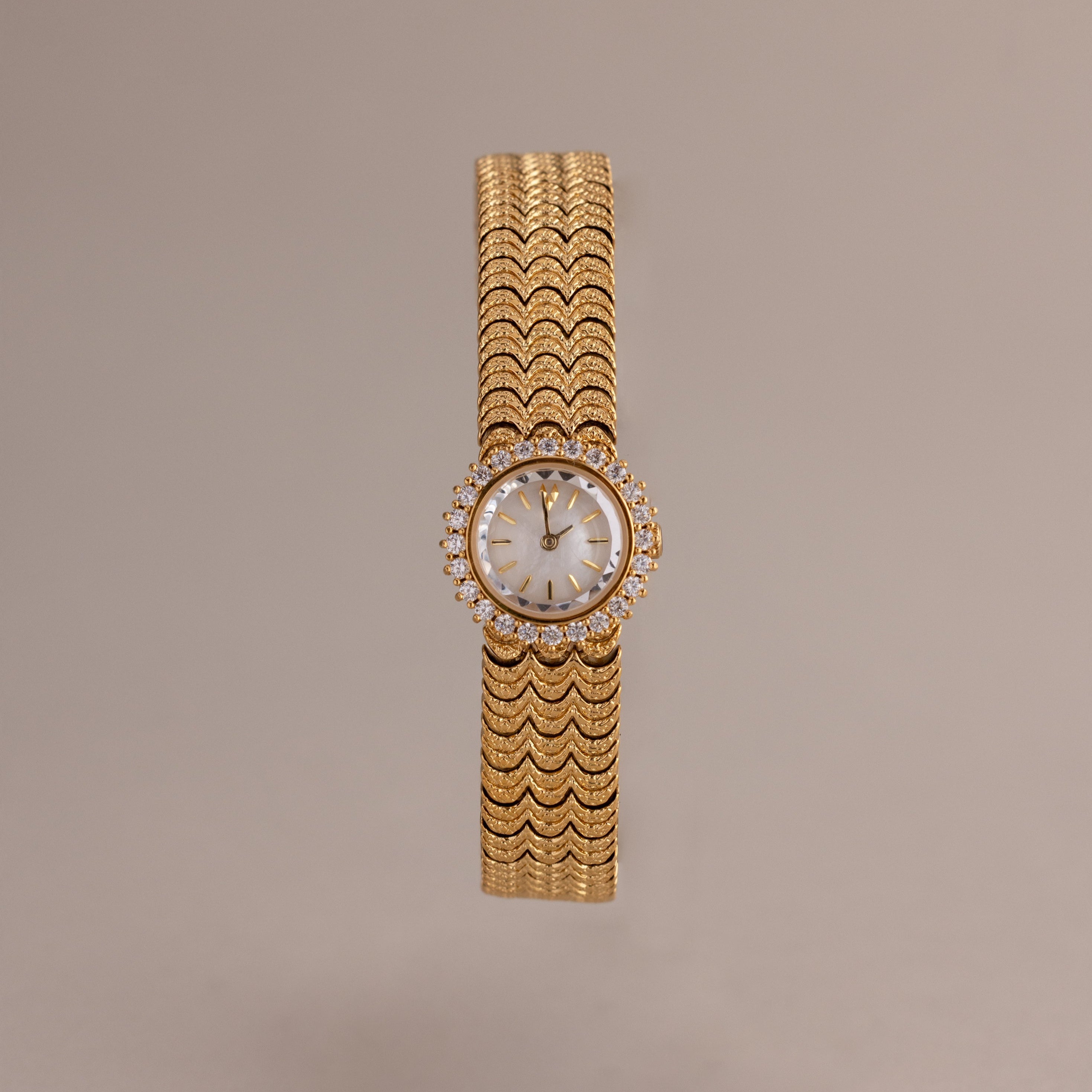 The Pave Scalloped Timepiece features a round face, diamond accents, and a scallop-link bracelet set against a neutral background.