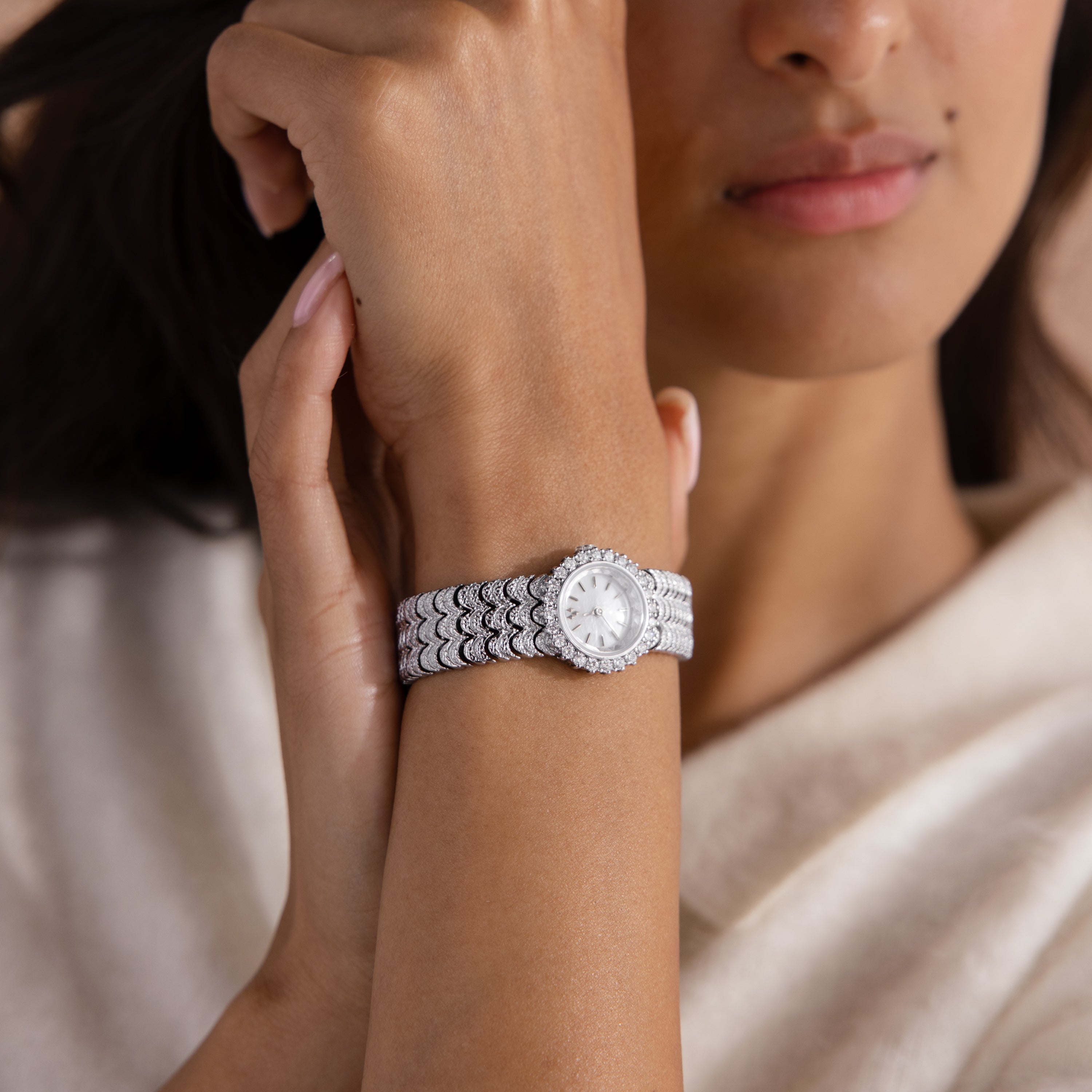A woman wearing the Pave Scalloped Timepiece, featuring a silver pavé bezel and a patterned band, holds her hand near her face.